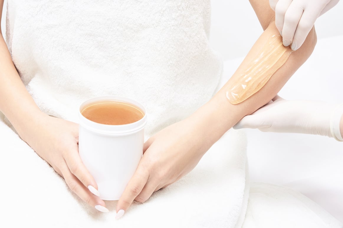 Woman Holding a Tub of Wax During Arm Hair Removal